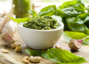 Basil pesto in a small bowl, with fresh basil leaves